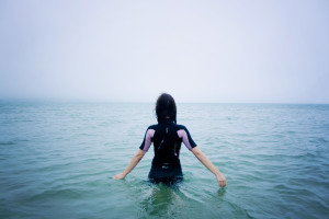 Teen girl wading into sea wearing wetsuit