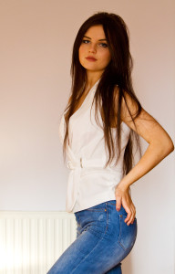 Teen girl with long brunette hair wearing white wrapover blouse and ripped jeans