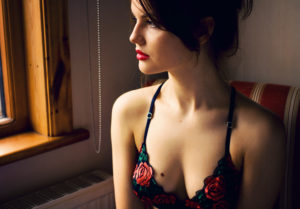 Girl wearing black and red embroidered bra looking out of window
