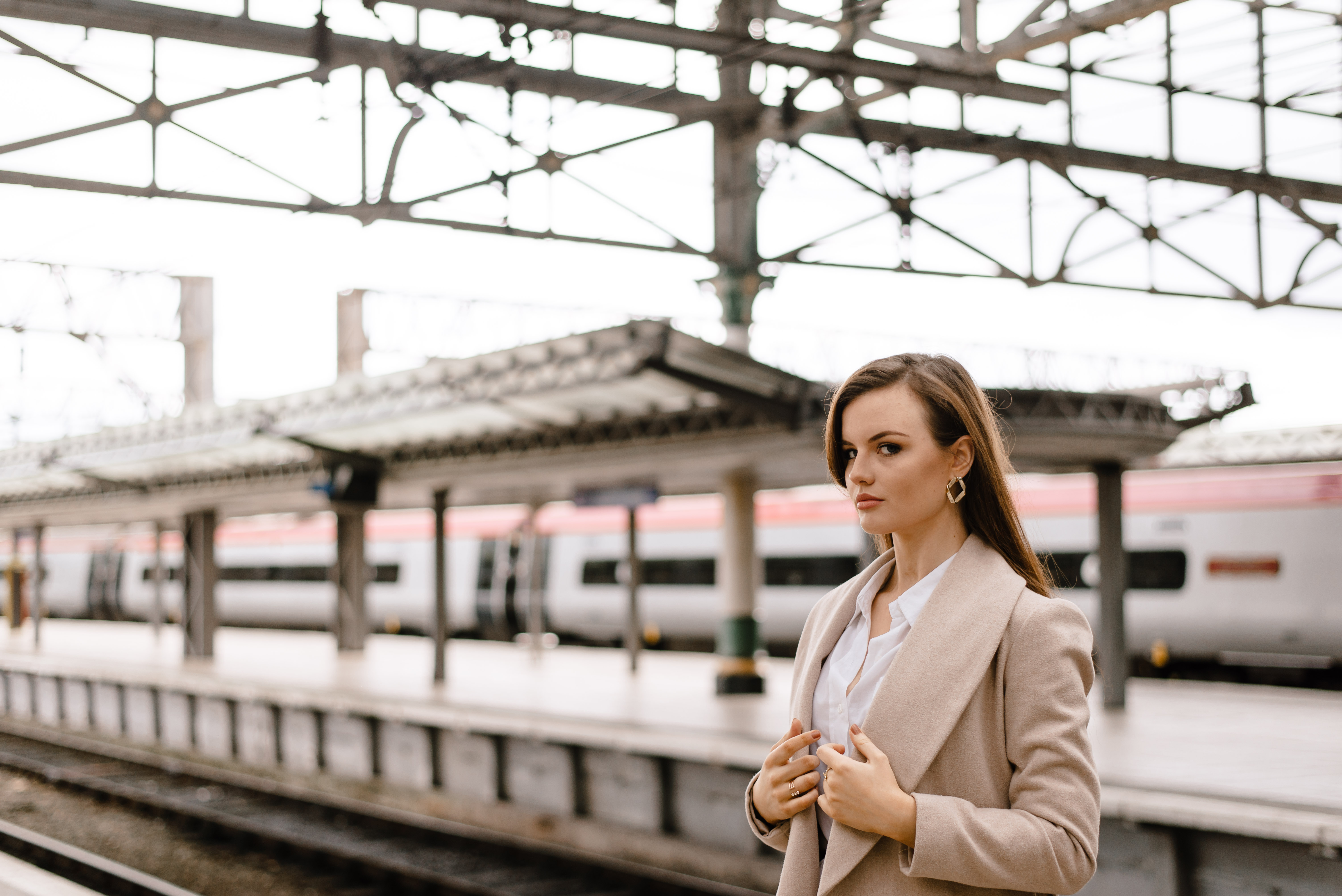 Girl wearing long beige coat standing on platform at train station Manchester England.