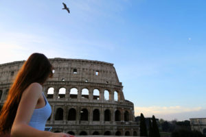 Girl standing in fron of Colosseum Rome Italy at sunrise. Blue sky.