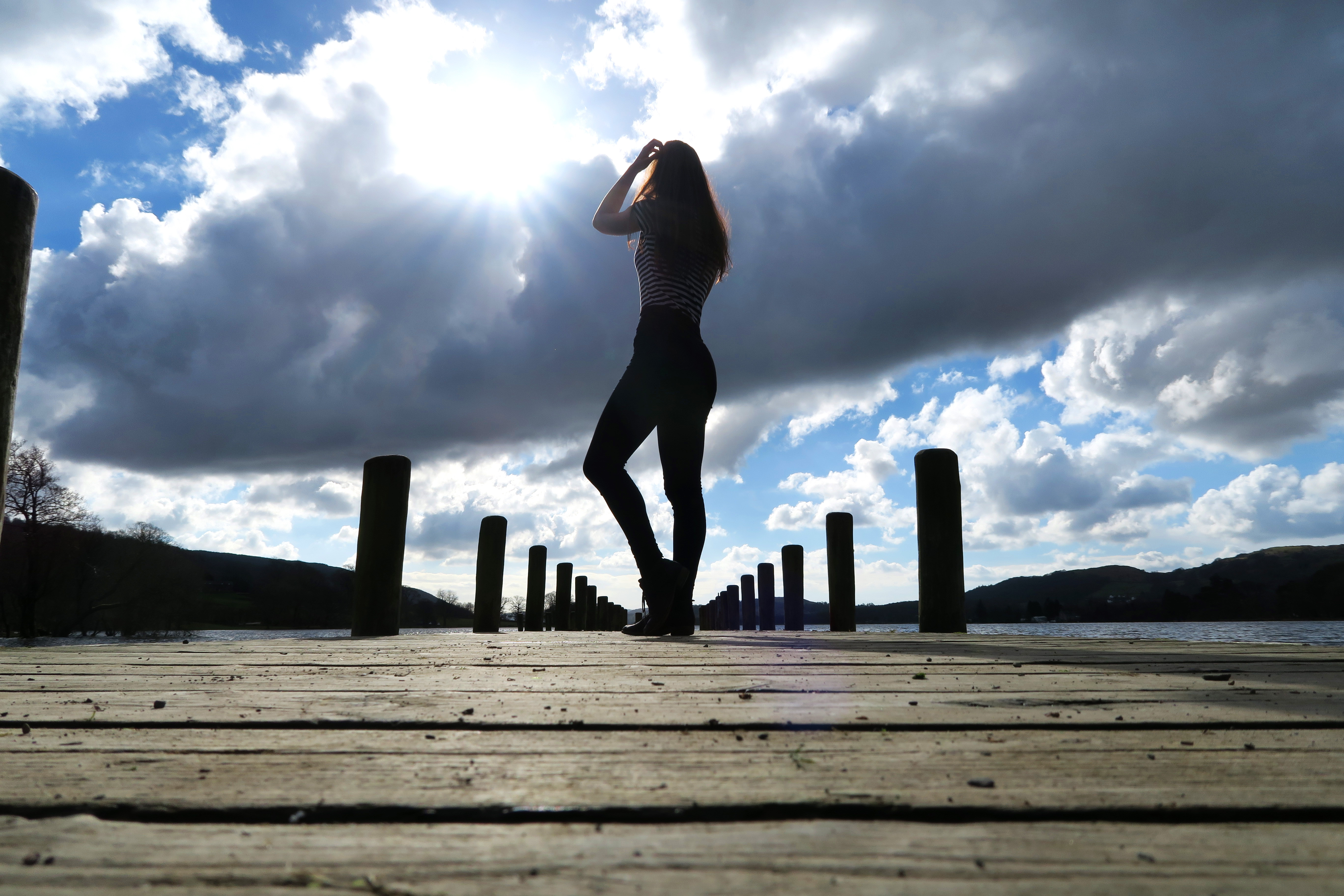Girl stood on wooden jetty. Blue sky background.
