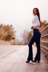 Female model standing on motorway bridge wearing flared denim jeans