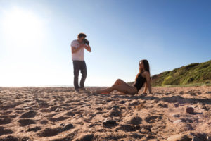 Photographer and model on beach shoot. Black swimsuit