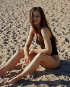 Young woman on sandy beach wearing black one-shoulder swimsuit