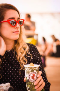 Young woman wearing red cateye sunglasses drinking coffee from paper cup