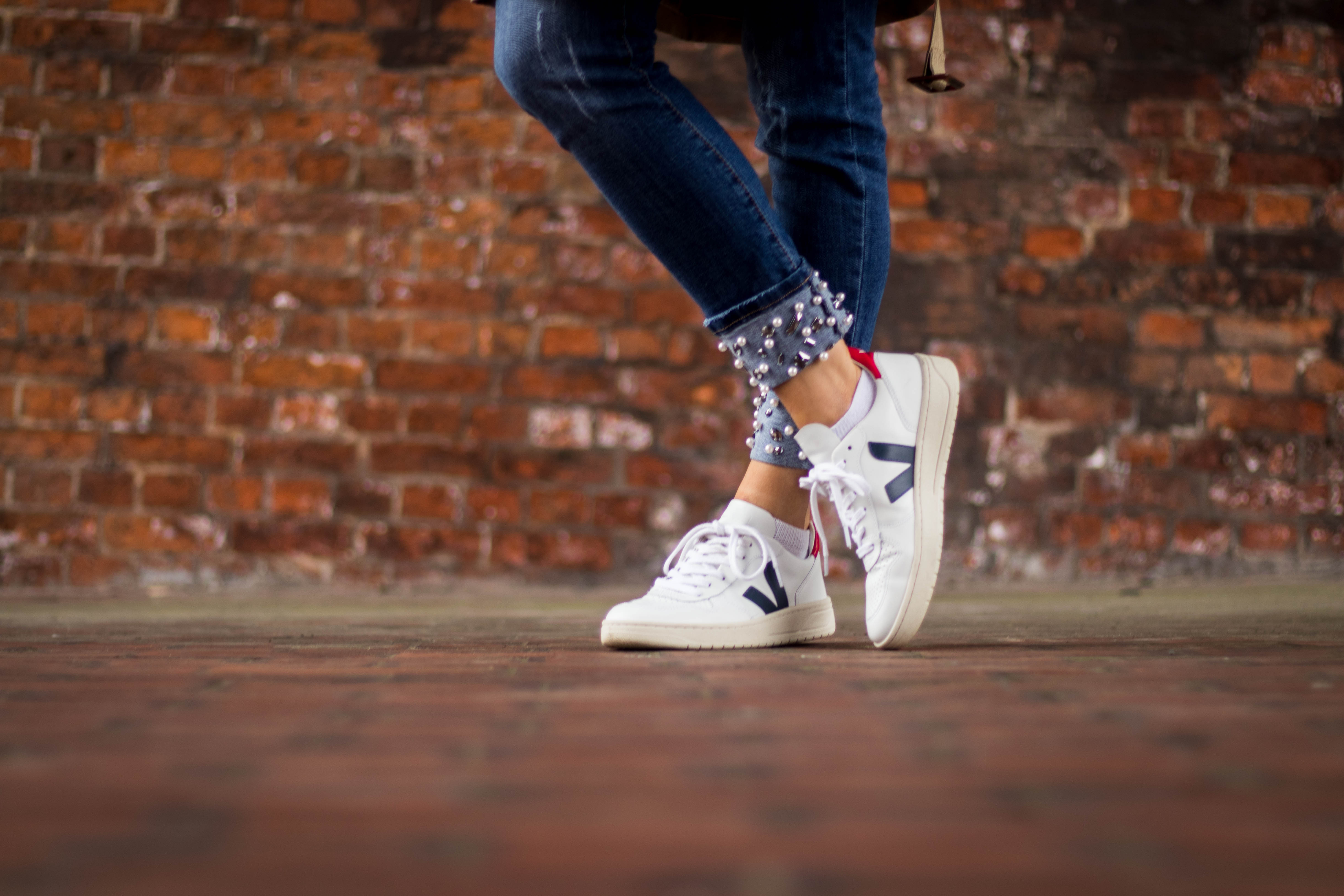 Blue jeans and Veja white trainers in front of wall